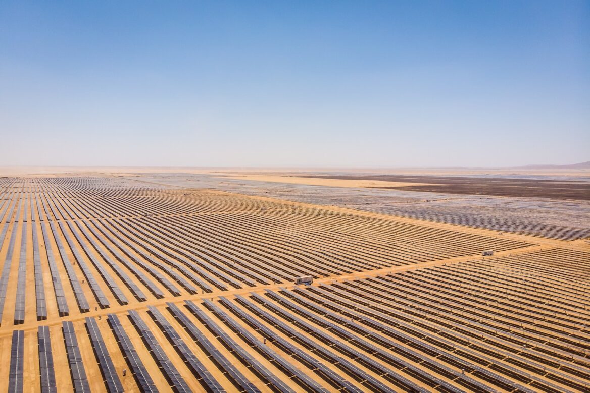 "Expansive solar farm in a desert landscape with long rows of solar panels under a clear blue sky, representing renewable energy generation in arid environments."