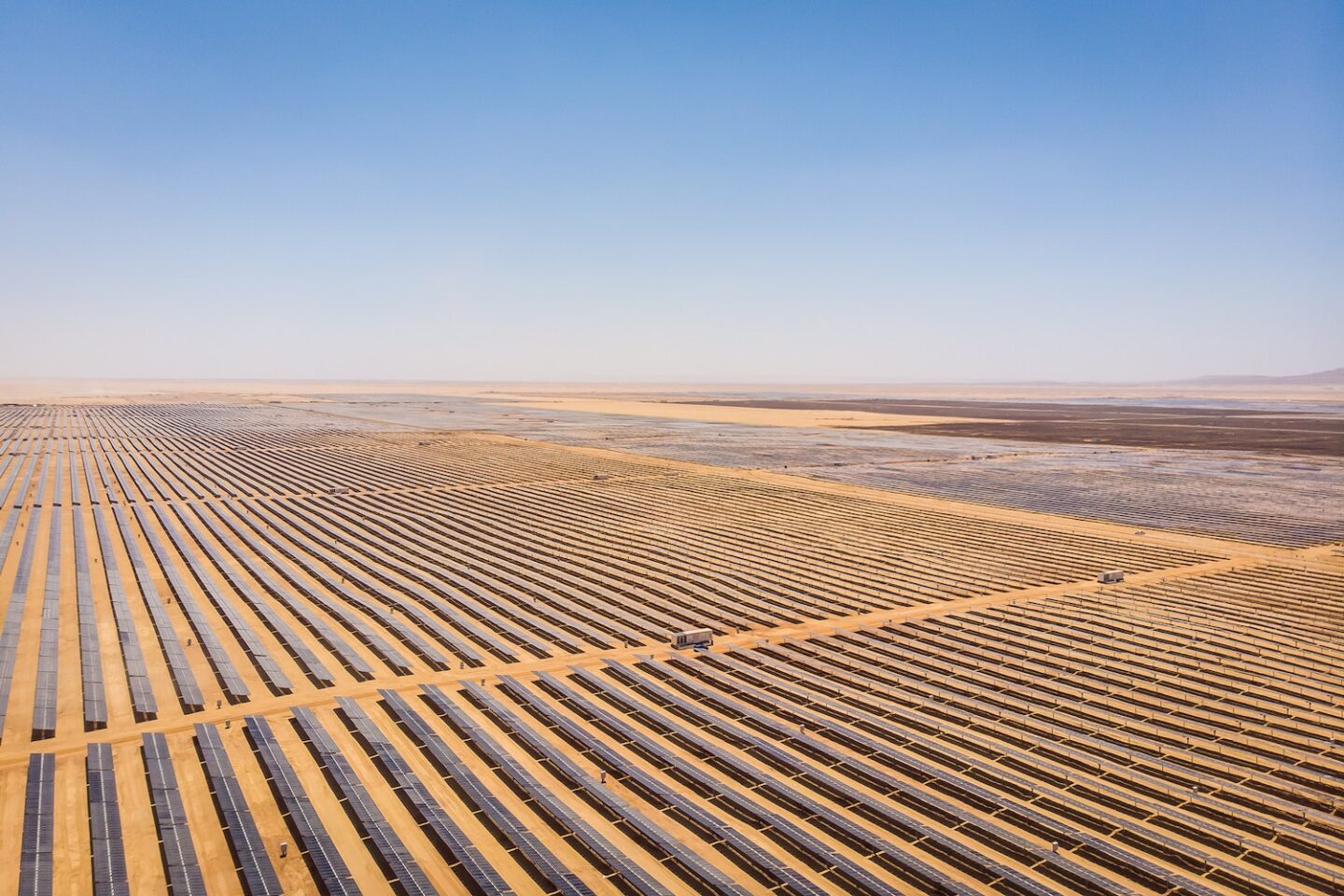 "Expansive solar farm in a desert landscape with long rows of solar panels under a clear blue sky, representing renewable energy generation in arid environments."