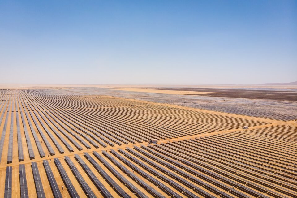 "Expansive solar farm in a desert landscape with long rows of solar panels under a clear blue sky, representing renewable energy generation in arid environments."