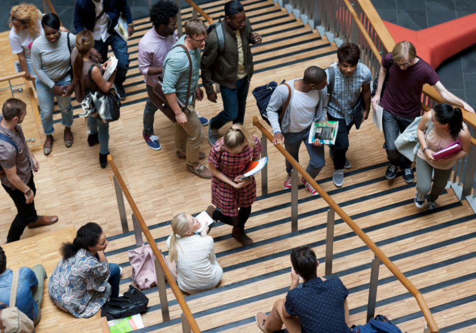 Students in a university library walking up and down some stairs carrying books and backpacks