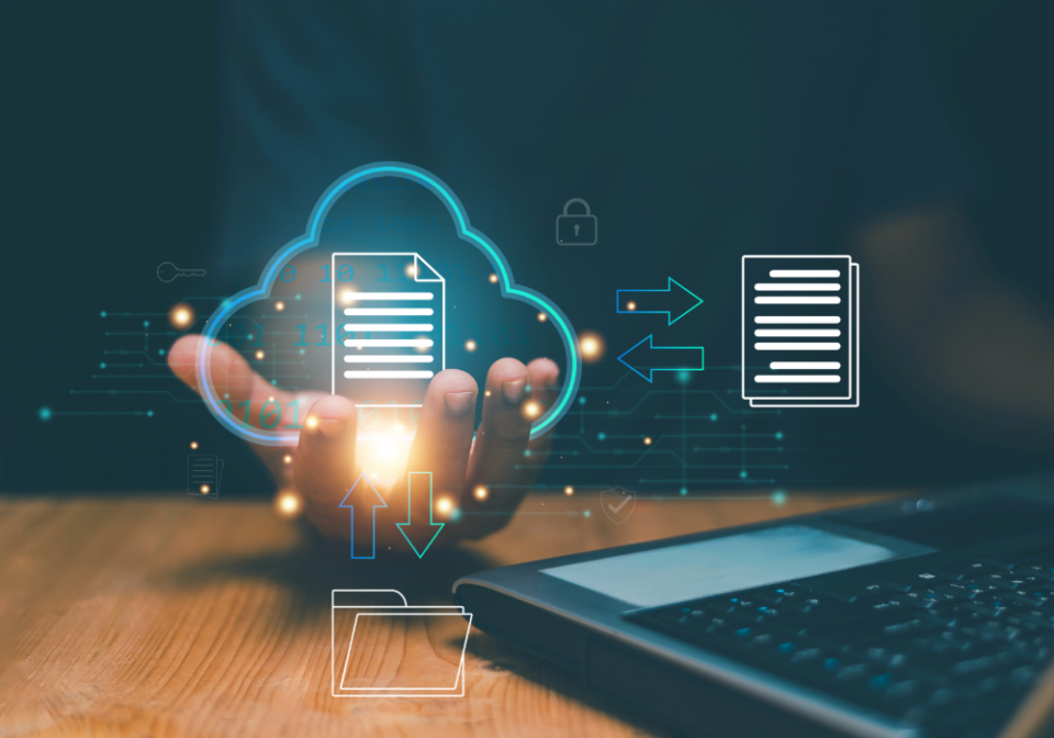 A hand holding a cloud icon with a file icon and arrows pointing to a folder left and below, a laptop sits on a table to the right
