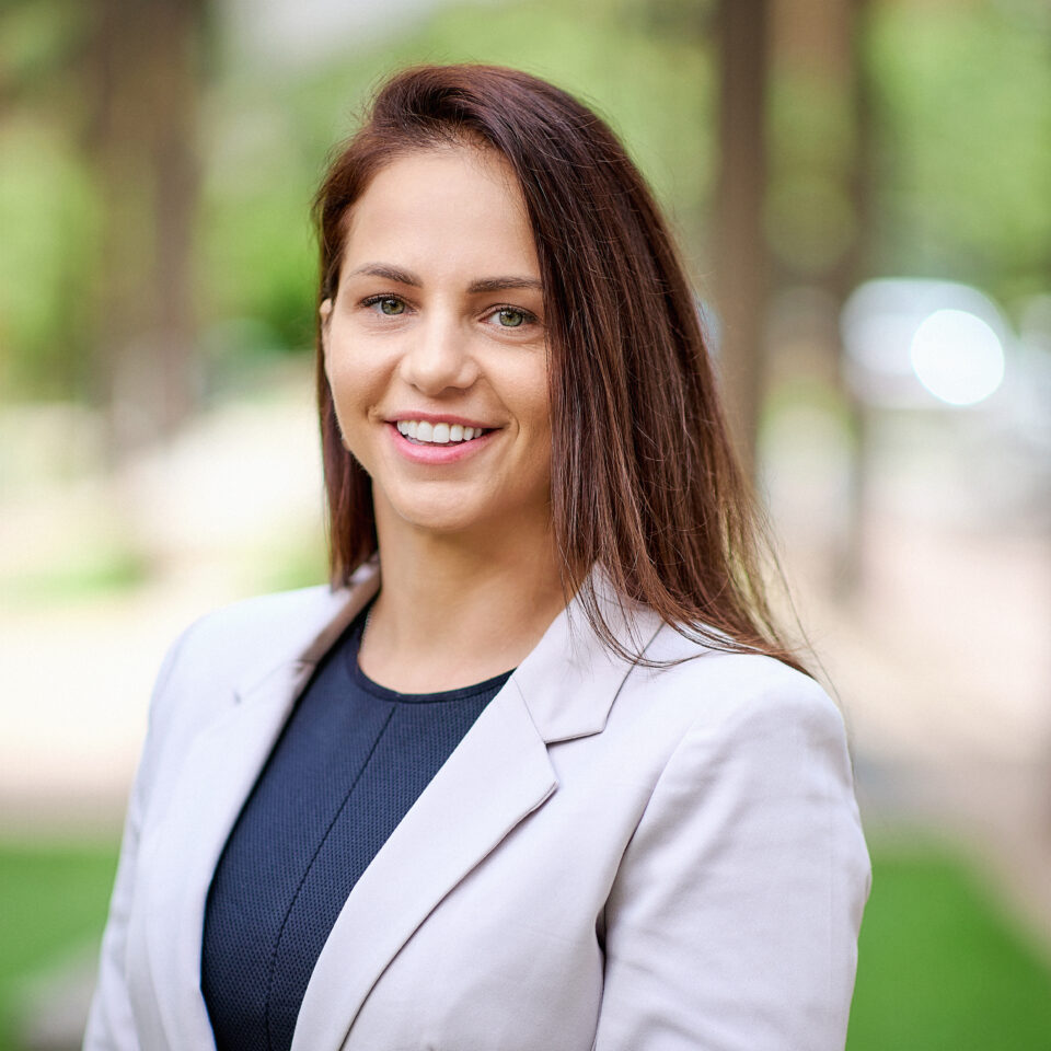 Suzana Trabuian Headshot - Suzana wears a dark shirt with a light coloured jacket, she has brown hair