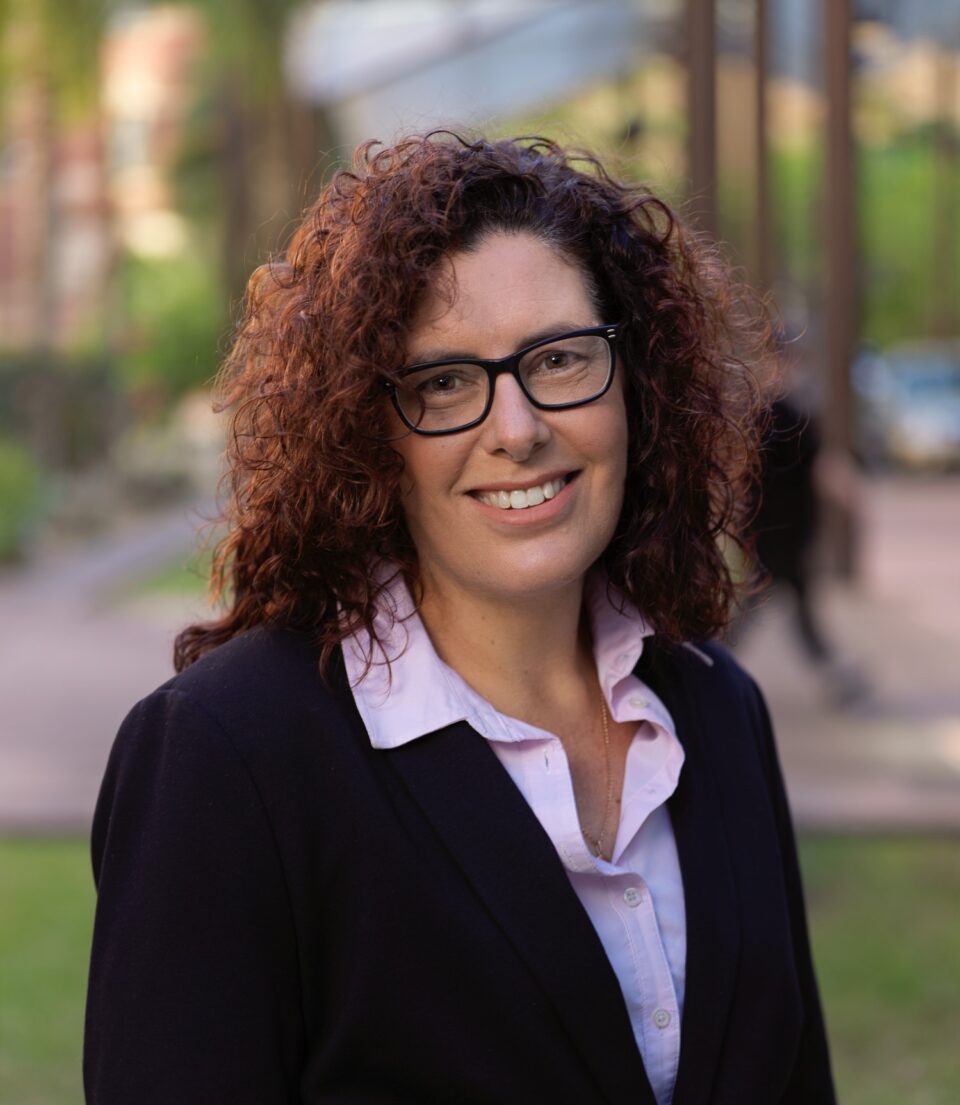 Mandi Swanson Headshot - Mandi wears a pink shirt and black blazer, has curly hair and wears glasses