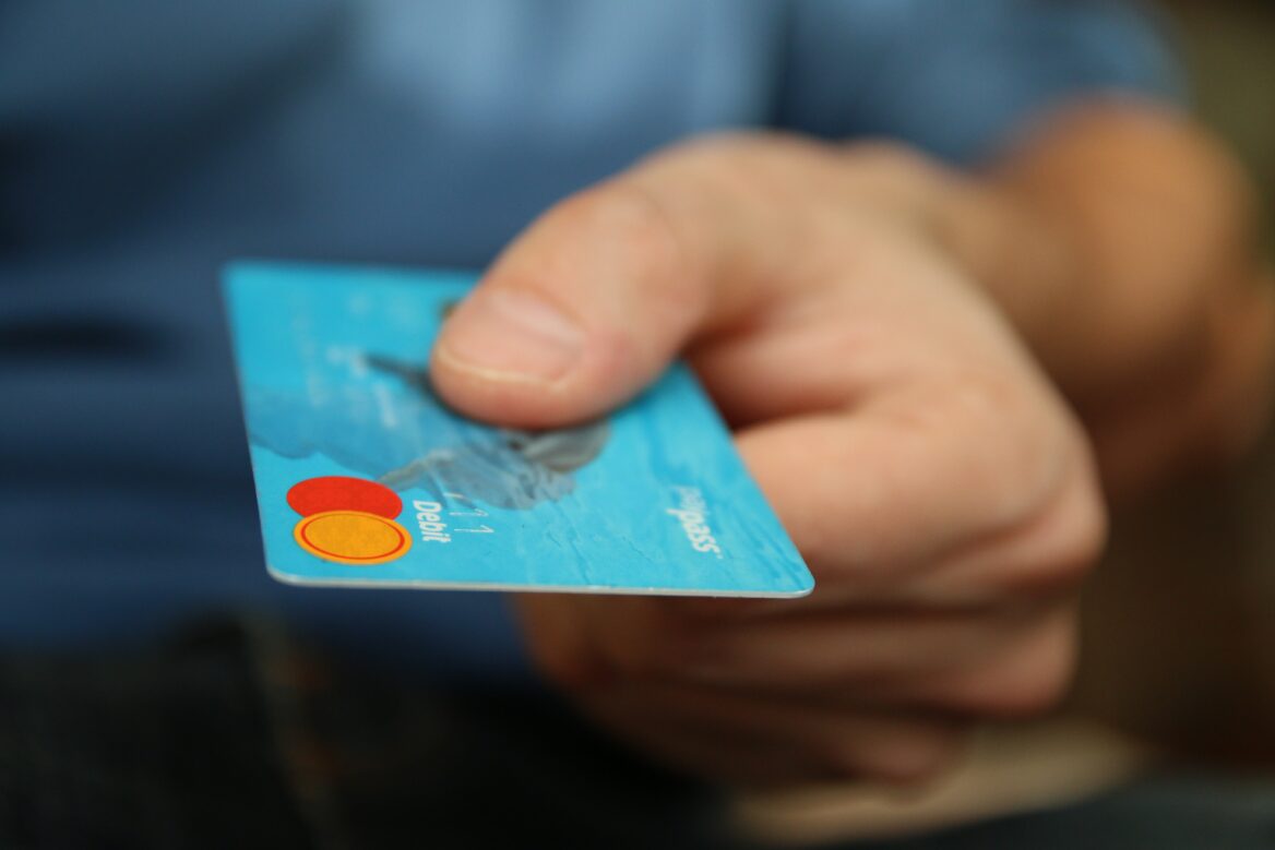 "Close-up of a hand holding a blue debit card with the Mastercard logo and abstract blue design, representing financial transactions."