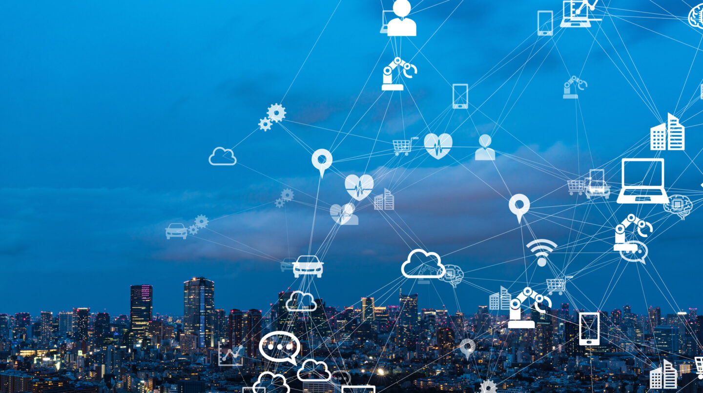 "Cityscape at dusk overlaid with interconnected white icons representing people, devices, and technology—such as Wi-Fi, smartphones, cars, and robotic arms—symbolising the Internet of Things (IoT) in a connected urban environment."