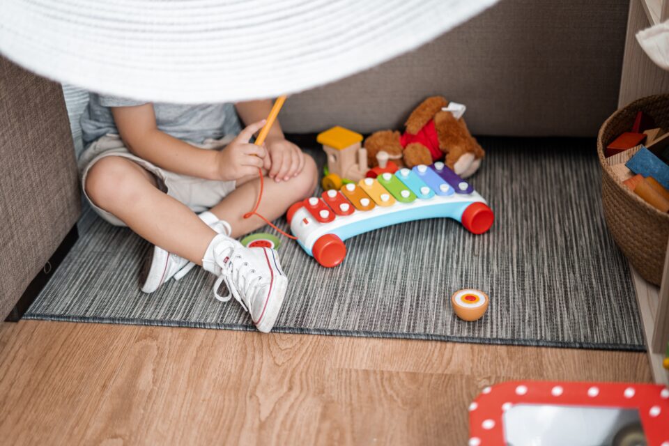 A small child sitting on the ground playing with a toy with a basket of toys to his left