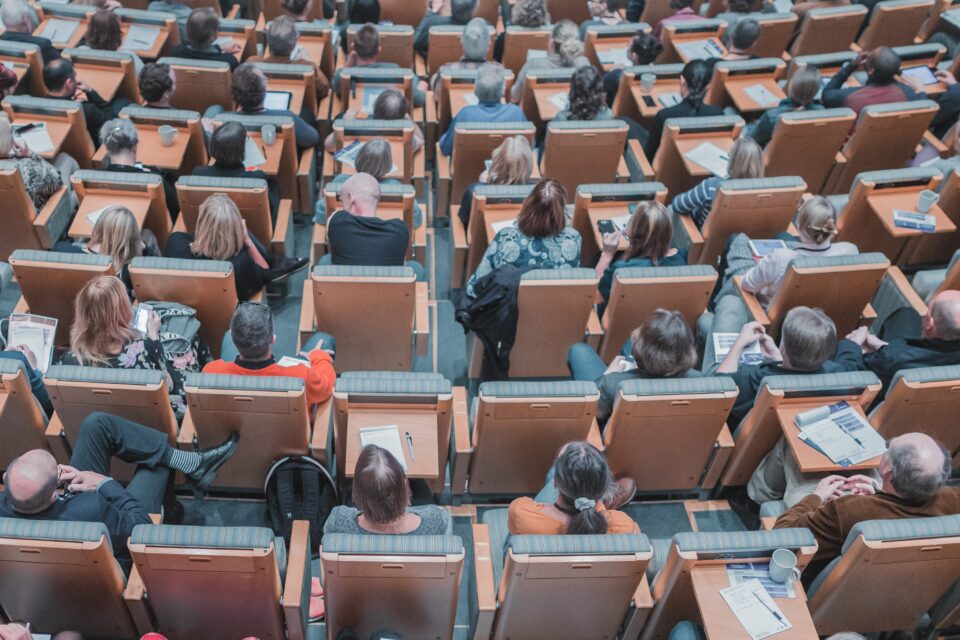 Photo taken from above showing a lecture theatre with people sitting listening intently and taking notes