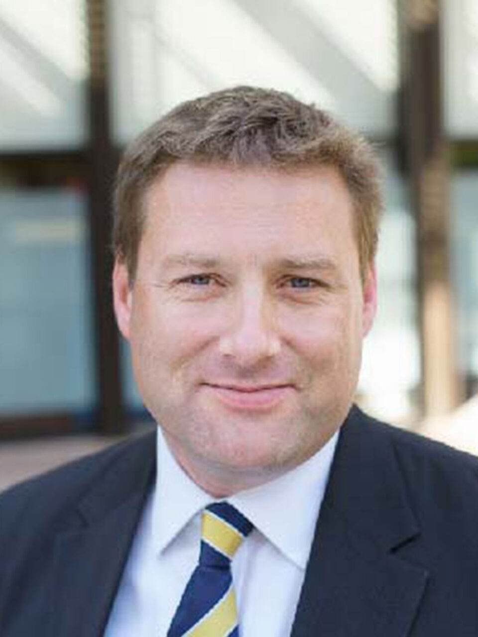 Neil Glentworth - Headshot - Neil wears a black jacket with a white shirt and a stripped tie.
