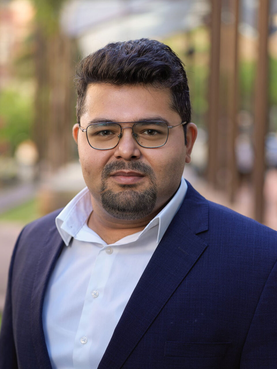 Nishant Monga Headshot - Nishand wears a white shirt and blue jacket, he has glasses and facial hair.